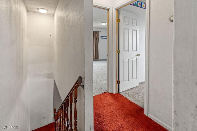 hall featuring an upstairs landing, carpet, and a textured ceiling