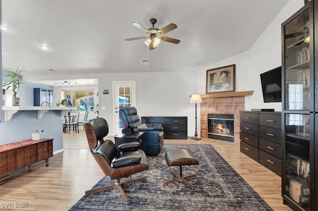 living area with visible vents, light wood-style flooring, a ceiling fan, and a tiled fireplace