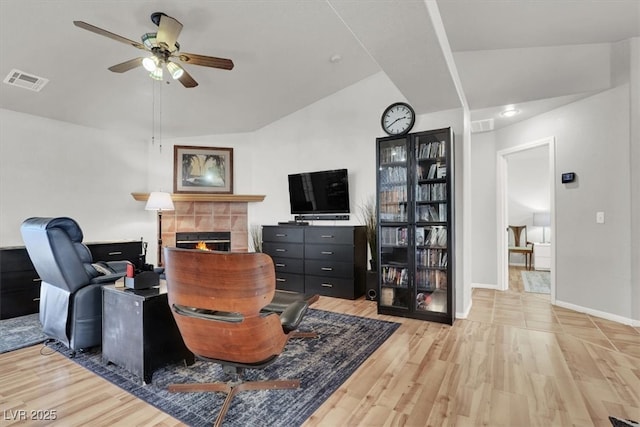 living area featuring a tiled fireplace, light wood-style flooring, a ceiling fan, and visible vents