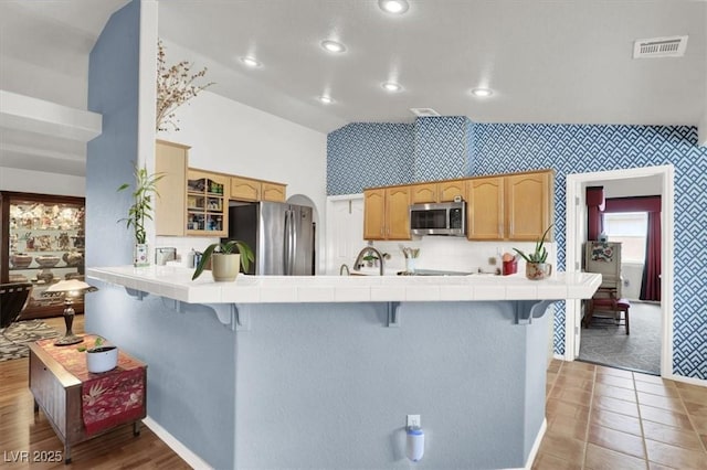 kitchen with a kitchen breakfast bar, tile countertops, visible vents, and stainless steel appliances