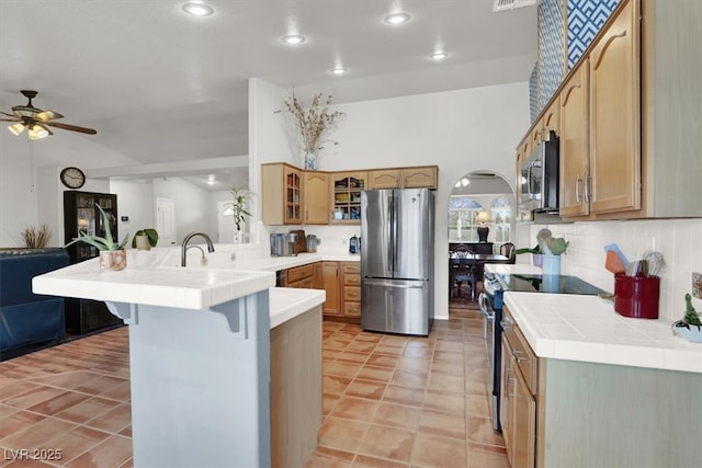 kitchen with glass insert cabinets, ceiling fan, a breakfast bar area, a peninsula, and stainless steel appliances