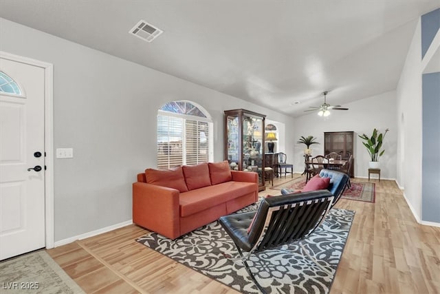 living area with visible vents, a ceiling fan, light wood-style floors, baseboards, and vaulted ceiling