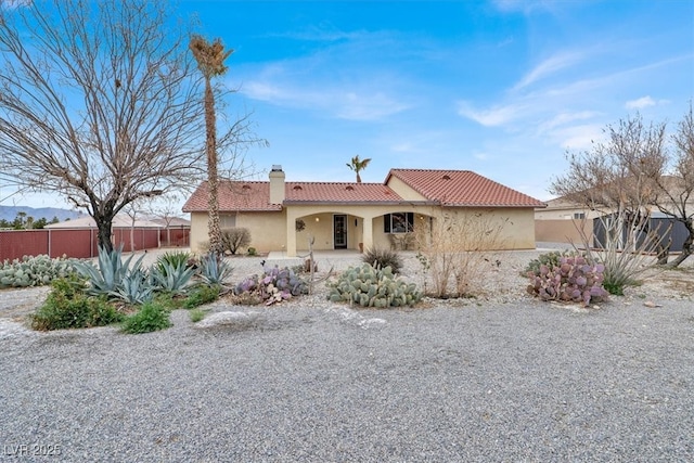 mediterranean / spanish-style home with stucco siding, fence, a chimney, and a tiled roof