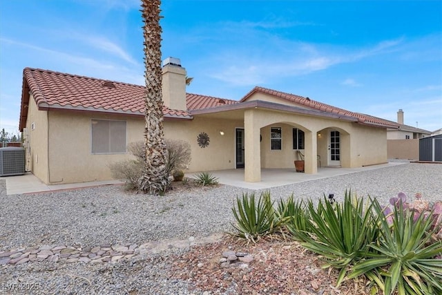 back of property featuring stucco siding, cooling unit, a chimney, and a tile roof