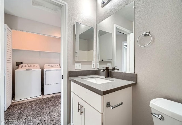 bathroom with vanity, washing machine and dryer, toilet, and a textured wall