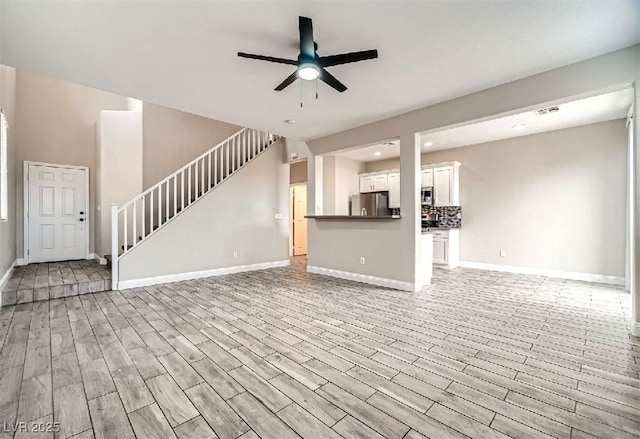 unfurnished living room with visible vents, baseboards, stairs, light wood-style flooring, and a ceiling fan