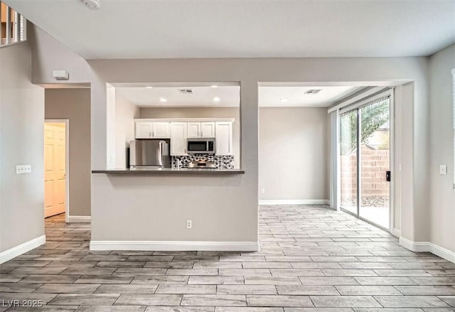 kitchen with wood finish floors, backsplash, appliances with stainless steel finishes, white cabinets, and baseboards