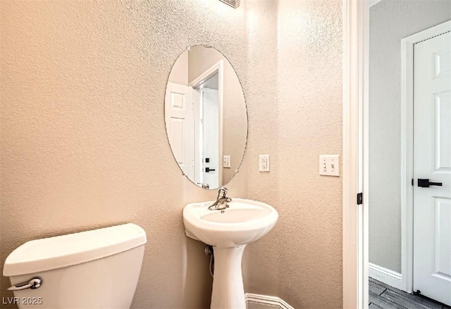 half bathroom with toilet and a textured wall