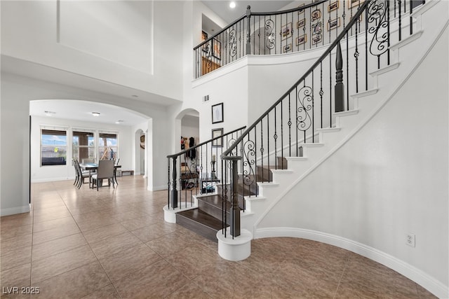 staircase featuring tile patterned floors, a high ceiling, baseboards, and arched walkways