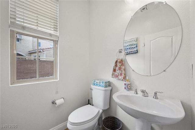 half bath with toilet, baseboards, and a sink