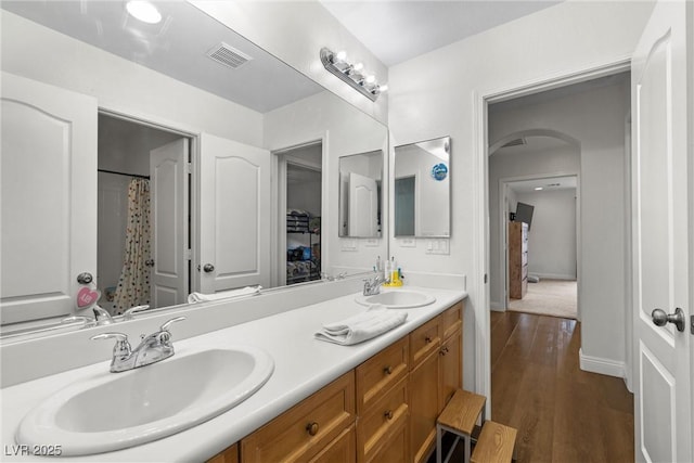 full bath featuring double vanity, wood finished floors, visible vents, and a sink