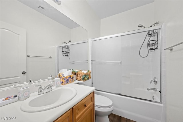 bathroom with visible vents, toilet, wood finished floors, combined bath / shower with glass door, and vanity