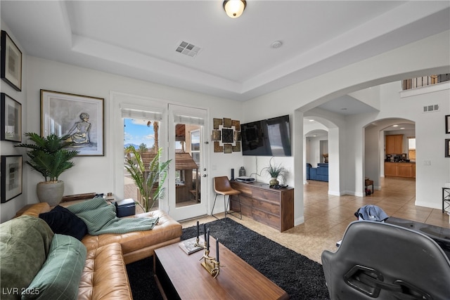 living room with arched walkways, visible vents, tile patterned floors, and a raised ceiling