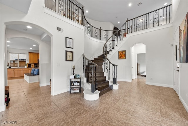 foyer with stairway, a high ceiling, arched walkways, and visible vents