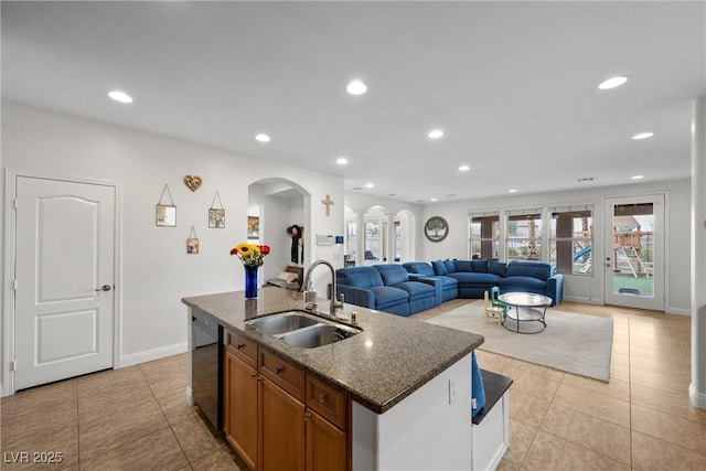 kitchen with arched walkways, brown cabinets, light tile patterned flooring, and a sink