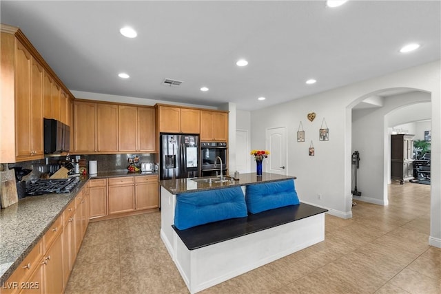 kitchen featuring visible vents, black appliances, a sink, dark stone counters, and arched walkways