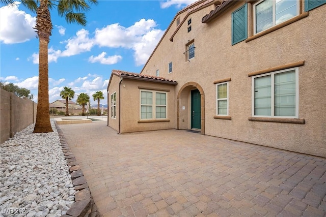 rear view of house with a tiled roof, fence, stucco siding, and a patio area