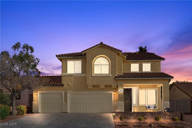 mediterranean / spanish house with stucco siding, a garage, concrete driveway, and a tiled roof