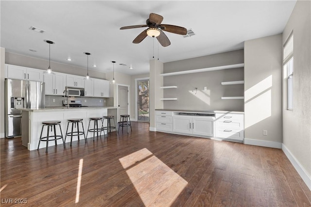 unfurnished living room with dark wood-style floors, visible vents, a healthy amount of sunlight, and a ceiling fan