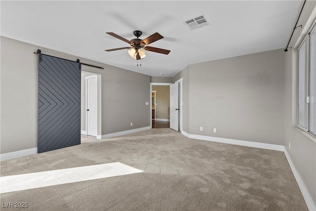 unfurnished bedroom featuring visible vents, light carpet, baseboards, and a barn door