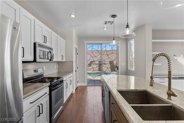 kitchen with a sink, tasteful backsplash, white cabinetry, stainless steel appliances, and hanging light fixtures