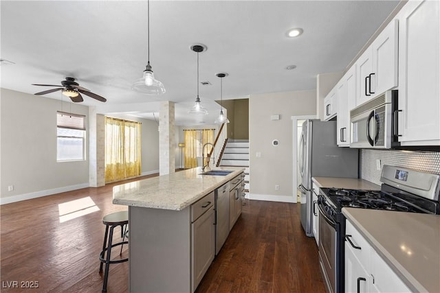 kitchen with a breakfast bar area, a sink, open floor plan, appliances with stainless steel finishes, and tasteful backsplash