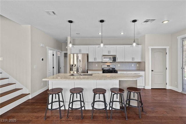 kitchen with visible vents, dark wood finished floors, a kitchen island with sink, appliances with stainless steel finishes, and backsplash