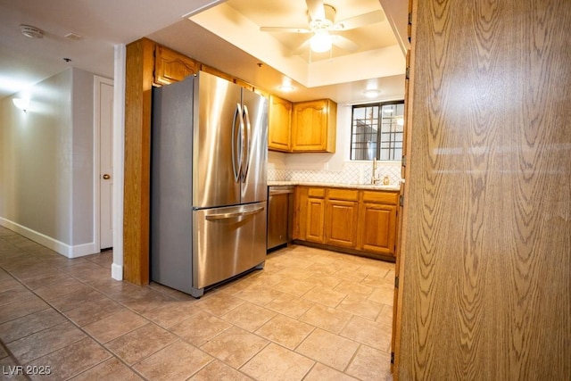 kitchen with a tray ceiling, tasteful backsplash, appliances with stainless steel finishes, light countertops, and ceiling fan