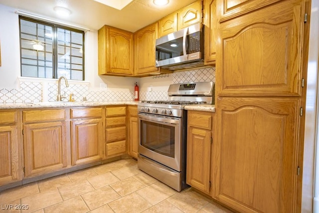 kitchen featuring a sink, stainless steel appliances, light stone countertops, and backsplash