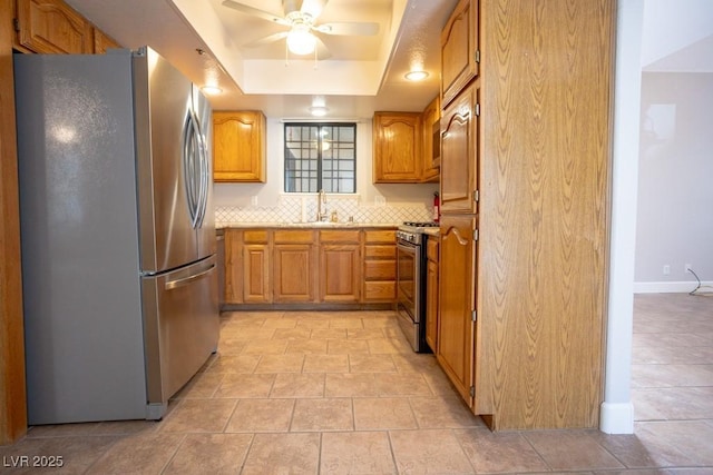 kitchen with a ceiling fan, a tray ceiling, a sink, decorative backsplash, and stainless steel appliances