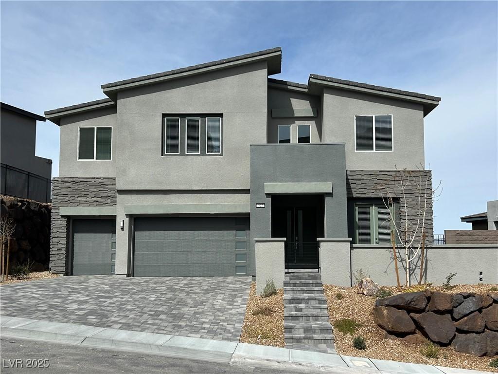 contemporary home with an attached garage, stone siding, driveway, and stucco siding