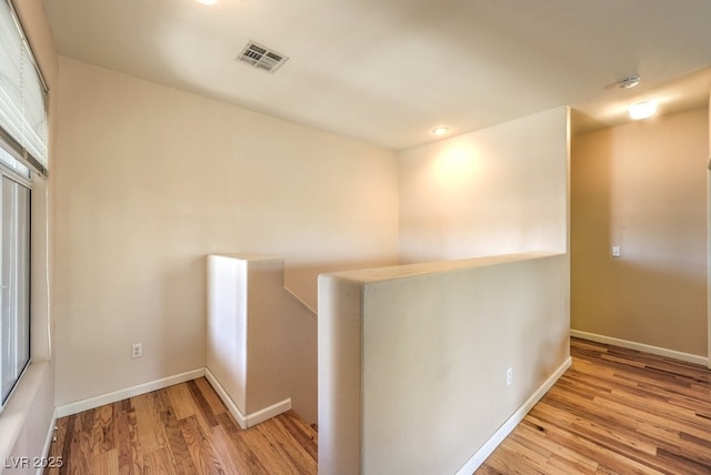 corridor with wood finished floors, an upstairs landing, visible vents, and baseboards