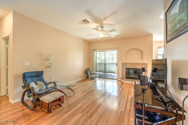 living room with visible vents, a ceiling fan, a glass covered fireplace, light wood-style floors, and baseboards