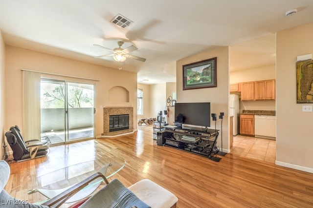 living room with light wood-type flooring, visible vents, a glass covered fireplace, baseboards, and ceiling fan