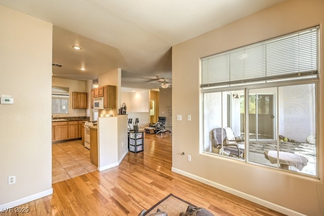 interior space with visible vents, baseboards, light wood-type flooring, white appliances, and a ceiling fan