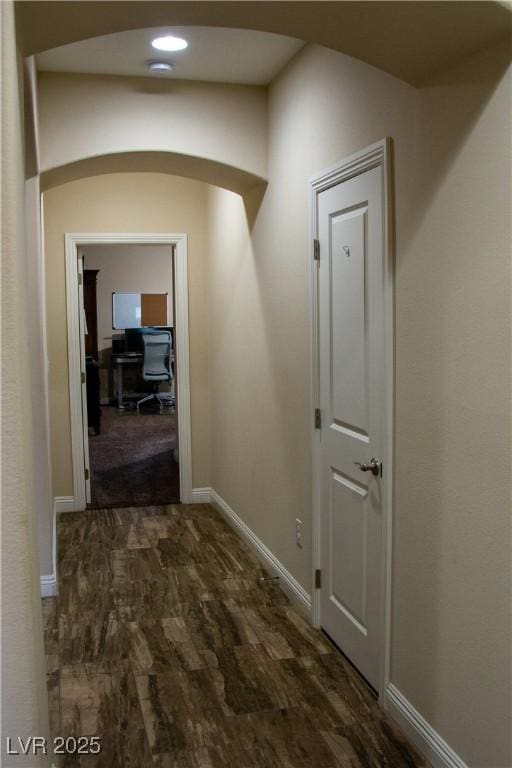 hall with wood finished floors, arched walkways, and baseboards