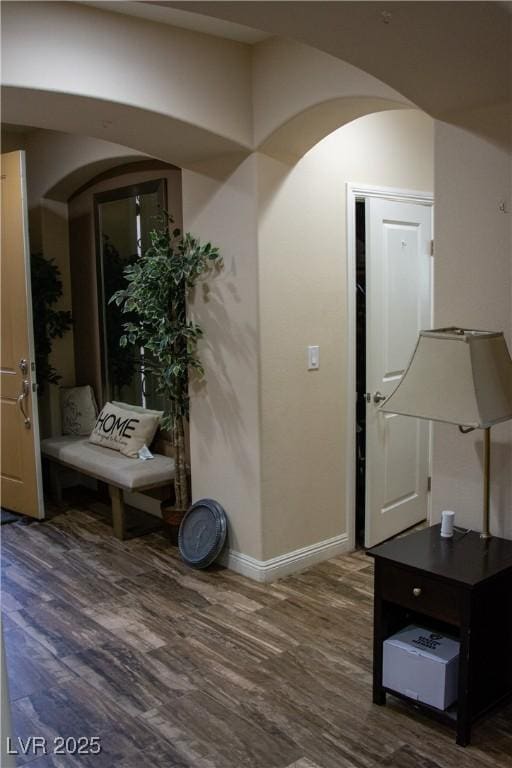 corridor with wood finished floors, arched walkways, and baseboards