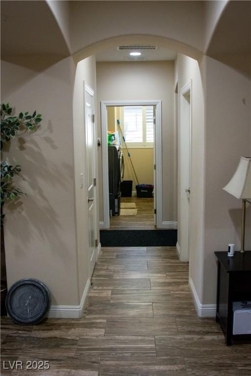 hallway with arched walkways, visible vents, baseboards, and wood finished floors