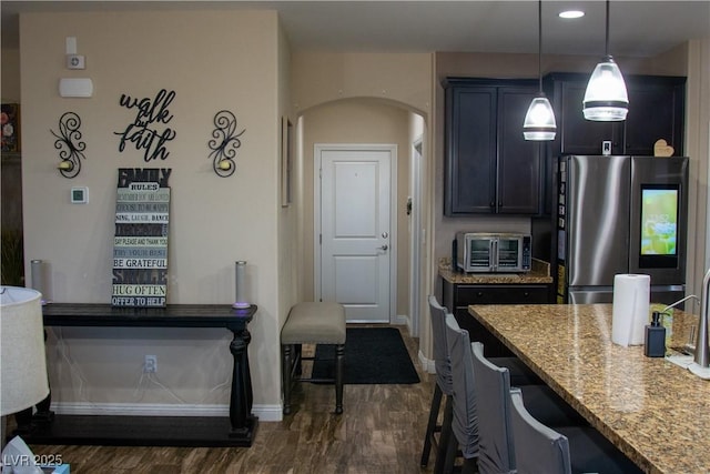 kitchen with light stone counters, dark wood-type flooring, smart refrigerator, a kitchen bar, and decorative light fixtures