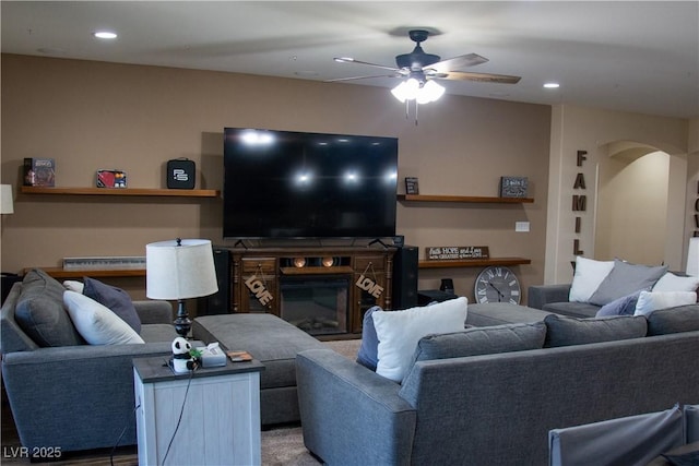 living room featuring arched walkways, a glass covered fireplace, recessed lighting, and ceiling fan