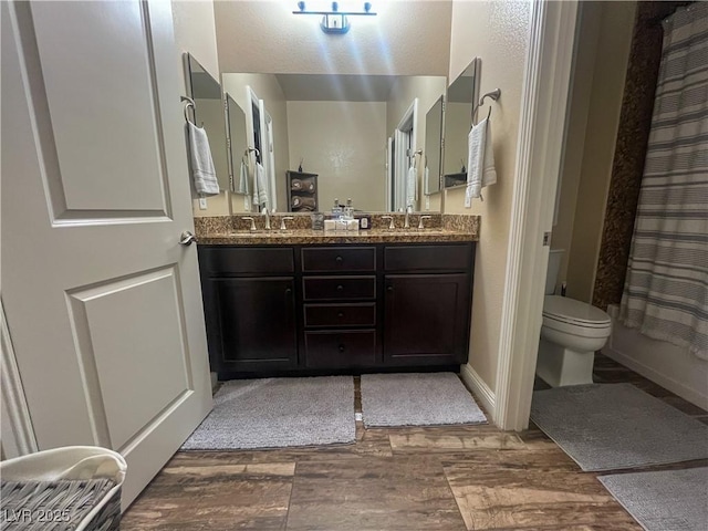 bathroom featuring double vanity, toilet, wood finished floors, and a sink