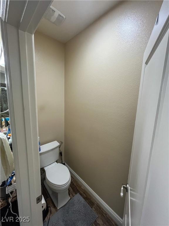 bathroom featuring toilet, wood finished floors, visible vents, and baseboards