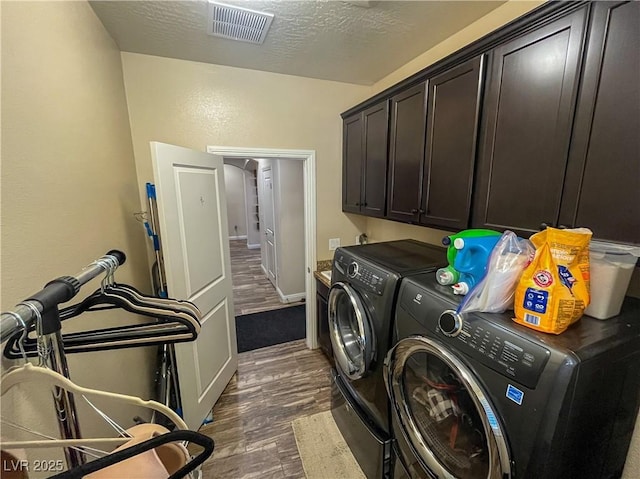 washroom with visible vents, a textured ceiling, washing machine and dryer, cabinet space, and dark wood-style flooring