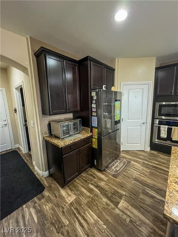 kitchen featuring light stone countertops, baseboards, dark wood finished floors, dark brown cabinets, and appliances with stainless steel finishes