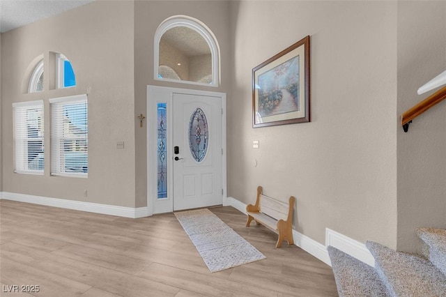 entryway with light wood-type flooring, baseboards, a towering ceiling, and stairway