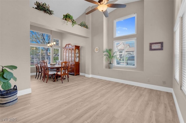 dining space featuring baseboards, light wood-type flooring, and a high ceiling