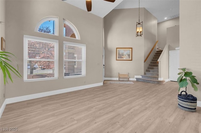 foyer with light wood finished floors, stairway, ceiling fan, and a towering ceiling