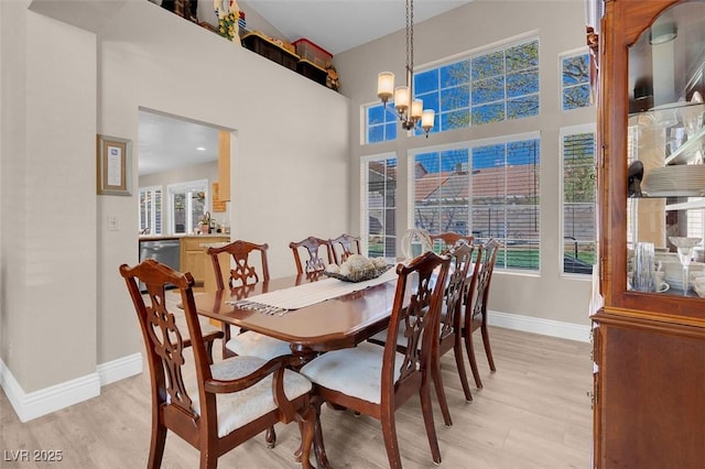 dining area with an inviting chandelier, a high ceiling, light wood-style floors, and baseboards