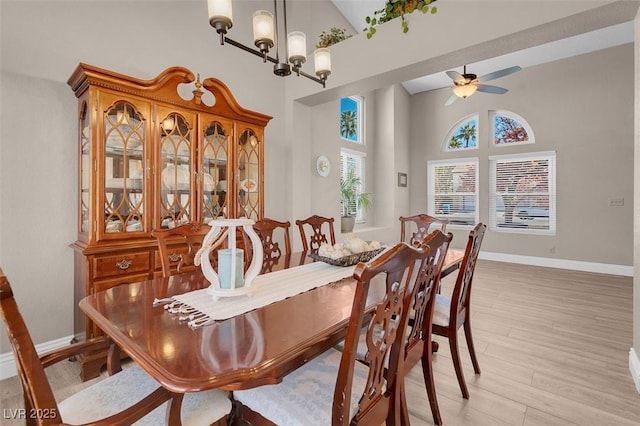 dining area with baseboards, ceiling fan with notable chandelier, a towering ceiling, and light wood finished floors