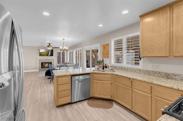 kitchen with a peninsula, light wood-style flooring, a sink, stainless steel appliances, and a glass covered fireplace